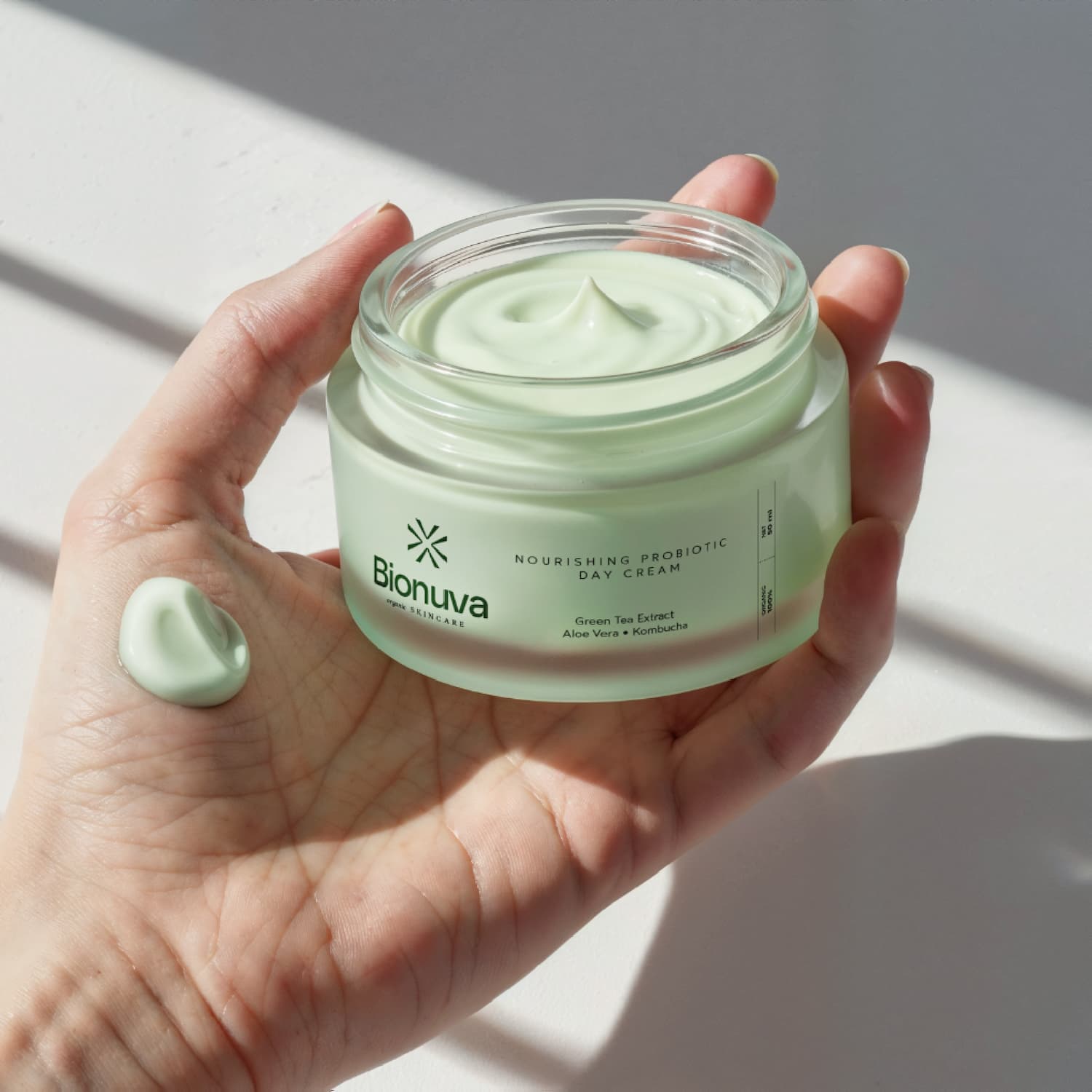 Product photography and label design for Bionuva day cream in a clear jar, shown in hand with applied texture. Designed byannas.com.