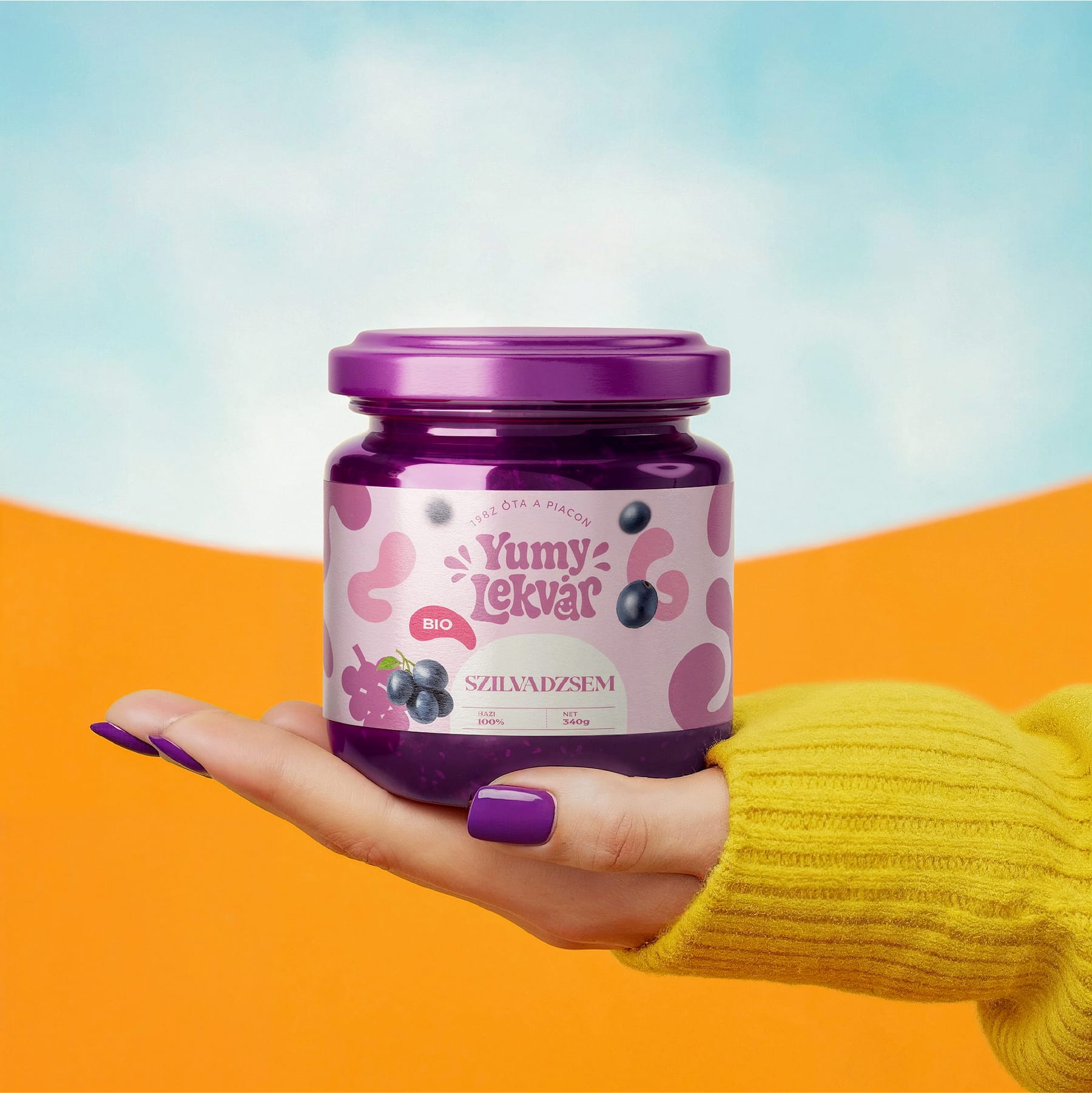 Hand holding a Yumy Lekvár plum jam jar against an orange and sky-blue backdrop: packaging design by byannas